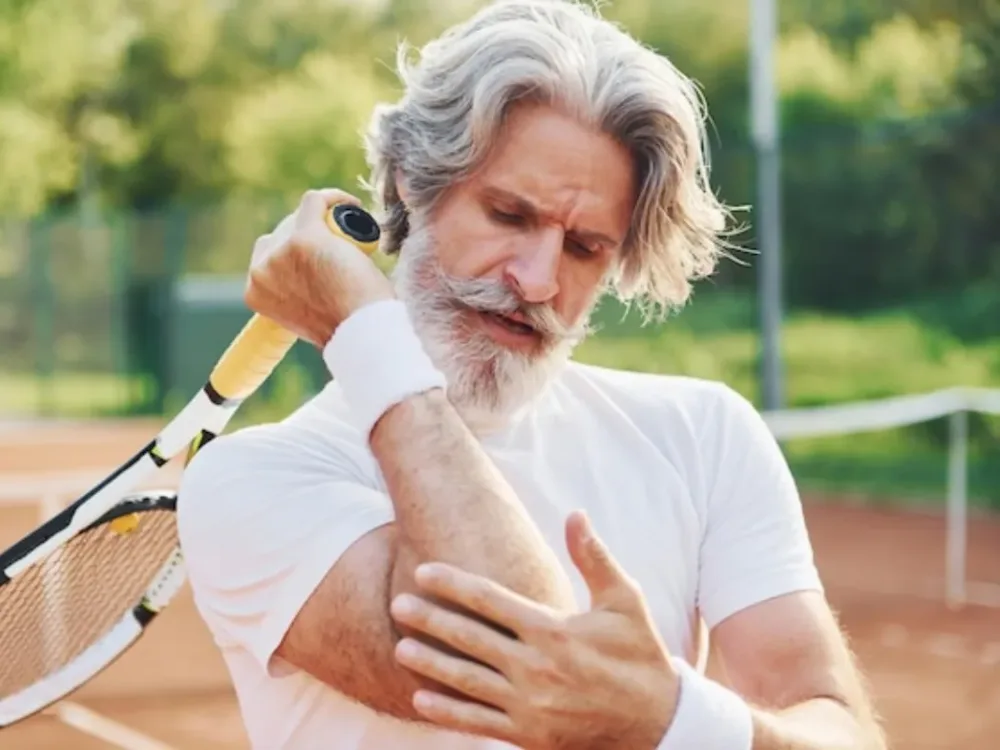 A tennis player on the court grips his elbow in pain, the sharp, specific ache that defines tennis elbow and golfer's elbow.