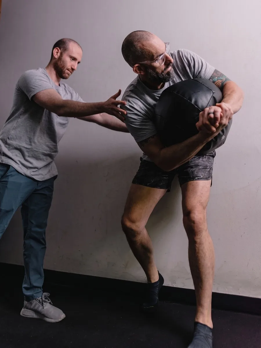 A trainer adjusts a client's positioning during a med-ball drill.